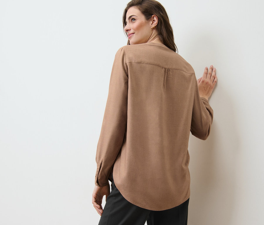 Žena opretá o stenu v tunikovej blúzke.