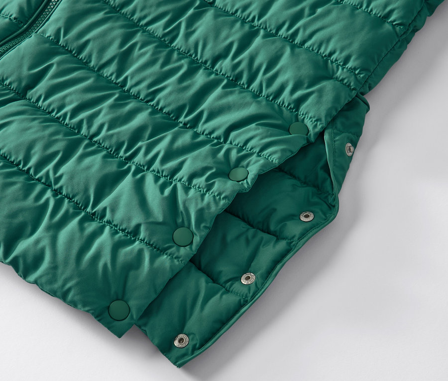 Detail zelenej prešívanej bundy s kapucňou a patentkami.