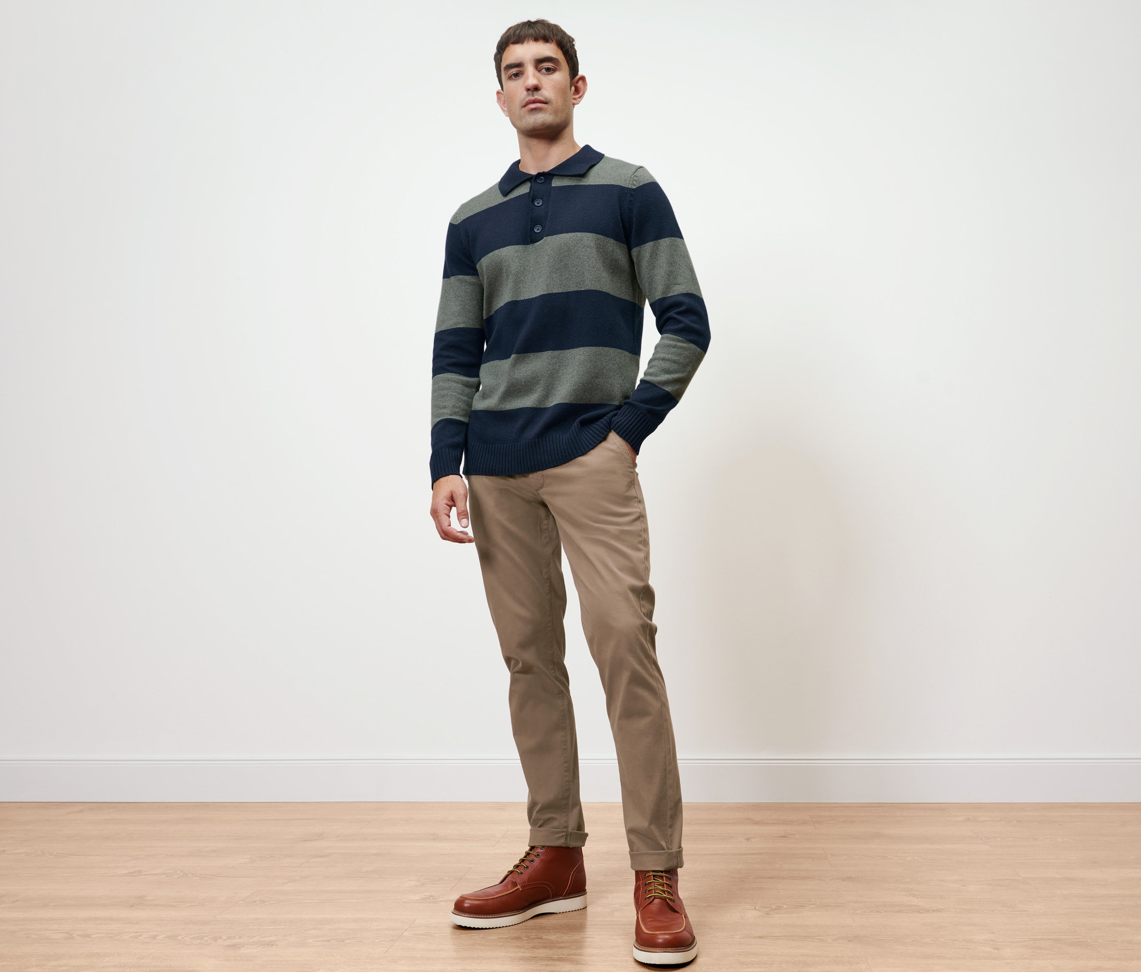 Muž pózuje v pulóvre a pieskových chino nohaviciach.