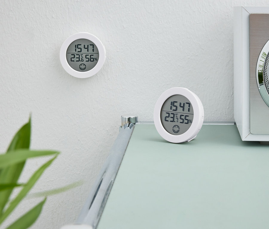 Dvoje biele digitálne hodiny. Jedny hodiny sú na stene. Druhé hodiny stoja na stole vedľa bieleho rádia.