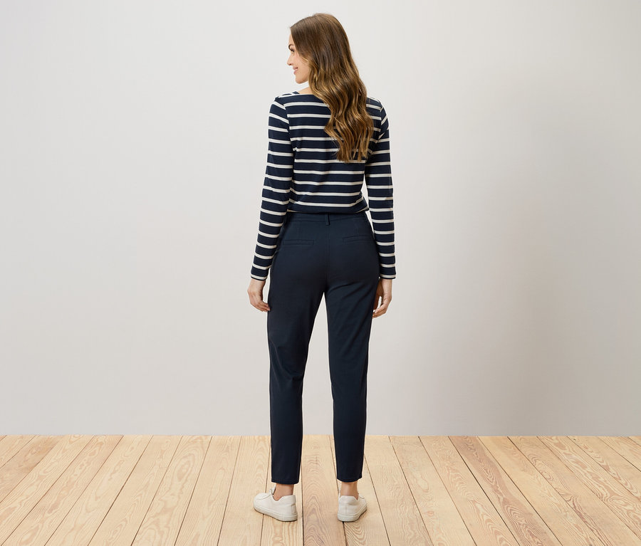 Zozadu vidíme ženu s hnedými vlasmi v tmavomodrých nohaviciach a pruhovanom tričku.