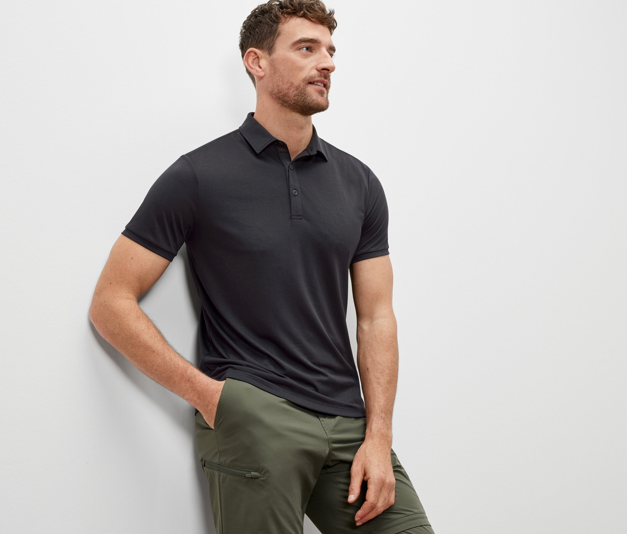 Muž opretý o stenu má na sebe antracitovú funkčnú polokošeľu.