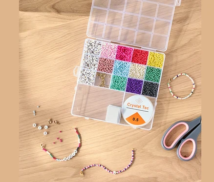 Otvorená súprava DIY korálok s farebnými korálkami, šnúrkou a nožnicami na drevenom stole.