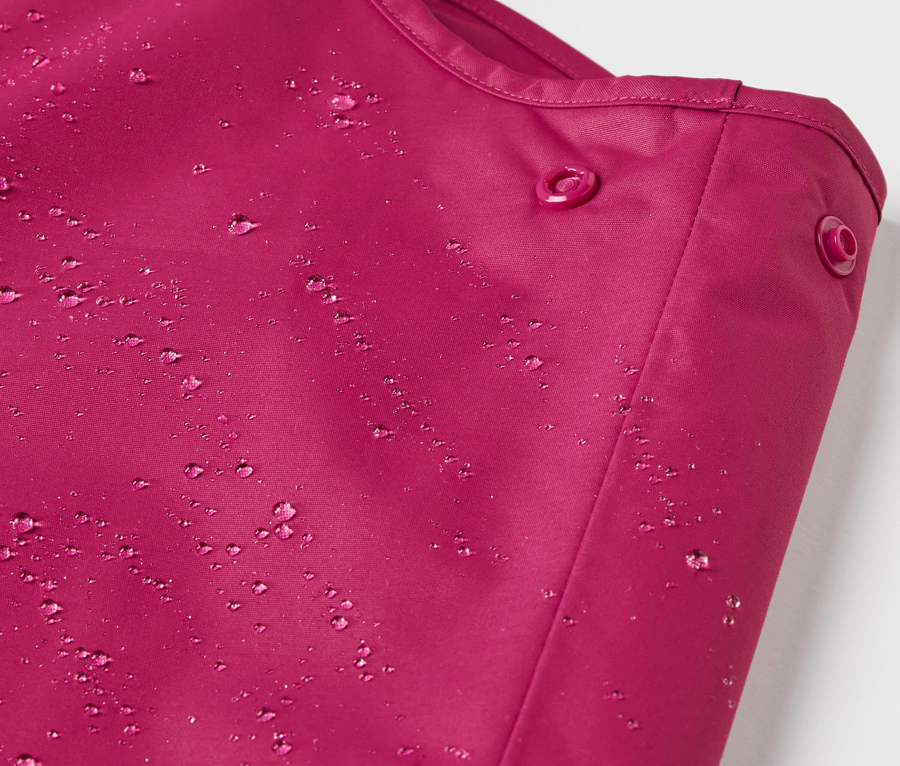 Detail detských termo nohavíc do dažďa vínovej farby s kvapkami vody.