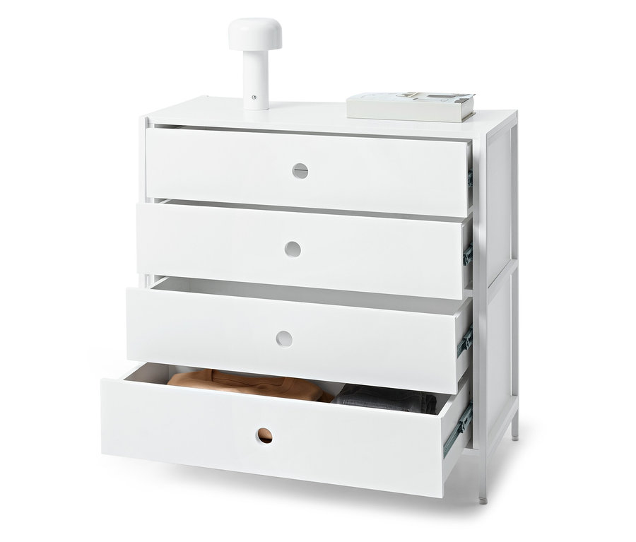 Biela komoda so štyrmi zásuvkami, z ktorých jedna je otvorená, na nej leží lampa a kniha.