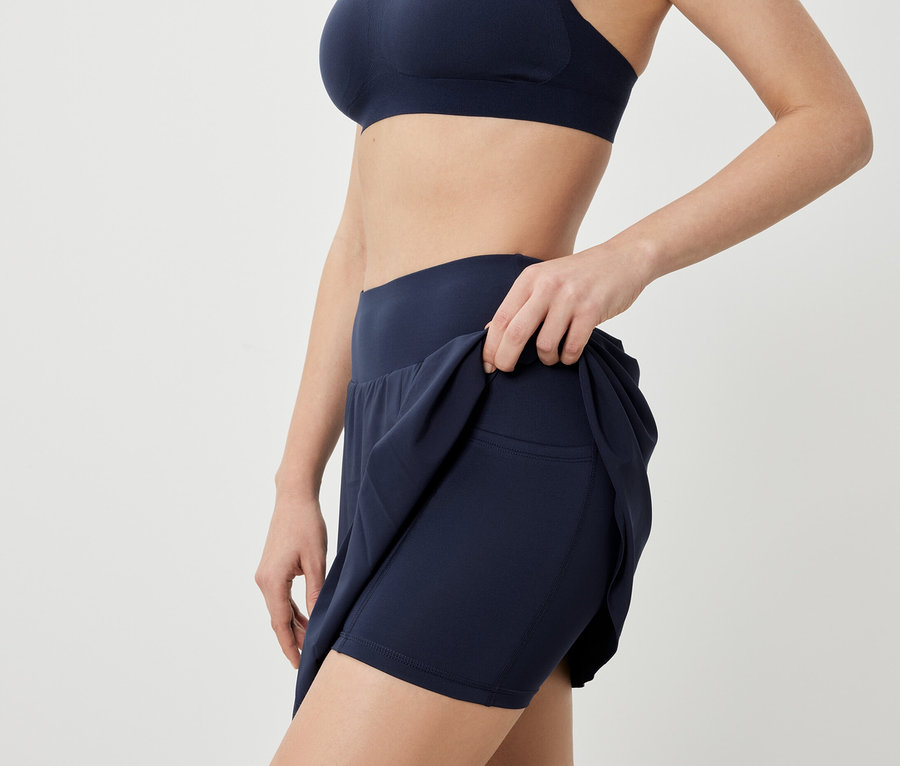 Žena pózuje v športovej podprsenke a tmavomodrej športovej sukni.