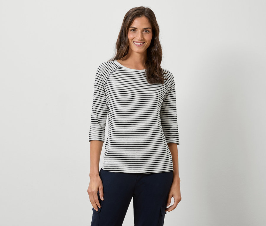 Žena má na sebe pásikavé tričko s dlhým rukávom a tmavomodré nohavice na bielom pozadí.