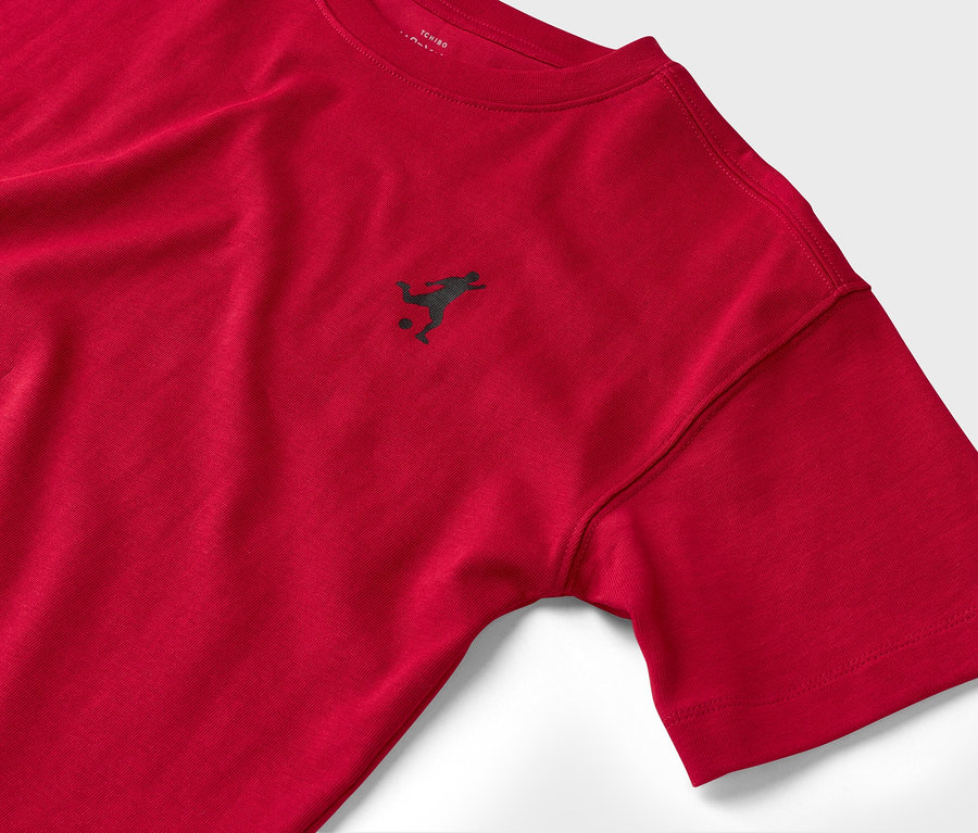 Detailný záber na červené tričko s krátkym rukávom a malým tmavým logom futbalistu.