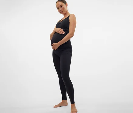 Tehotná žena v čiernom tope a skinny legínach MAMALICIOUS »MLTIA JEANNE« si drží brucho.
