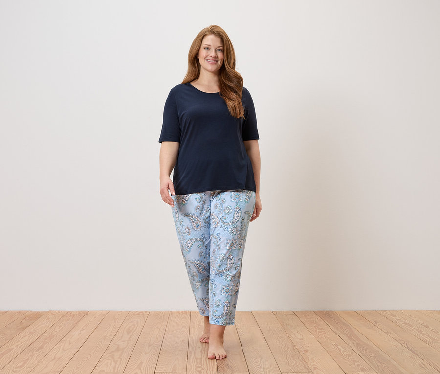 Žena kráča naboso v tmavomodrom tope a svetlomodrých nohaviciach s paisley vzorom.