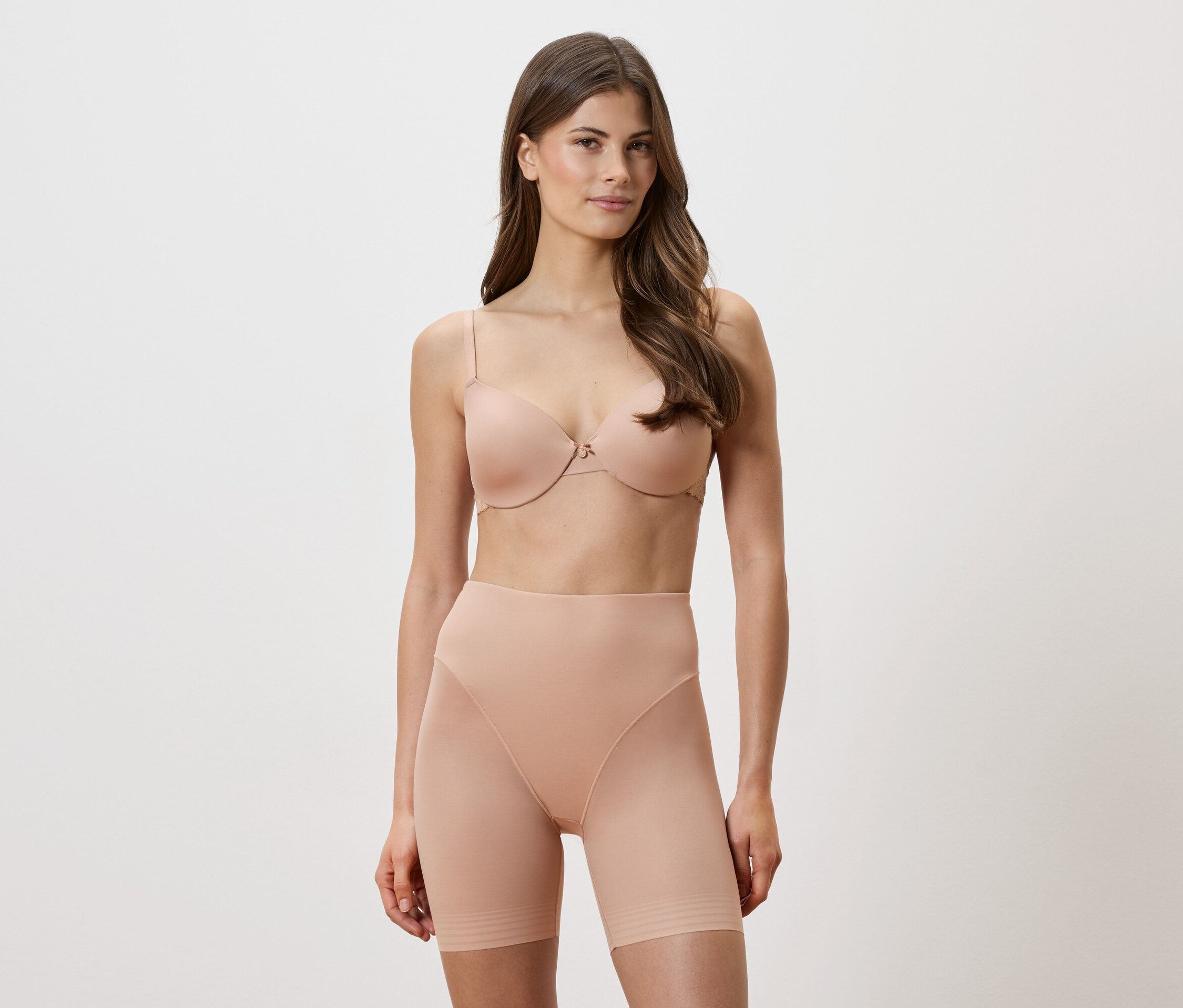 Žena má na sebe telovú podprsenku a tvarujúce šortky na bielom pozadí.