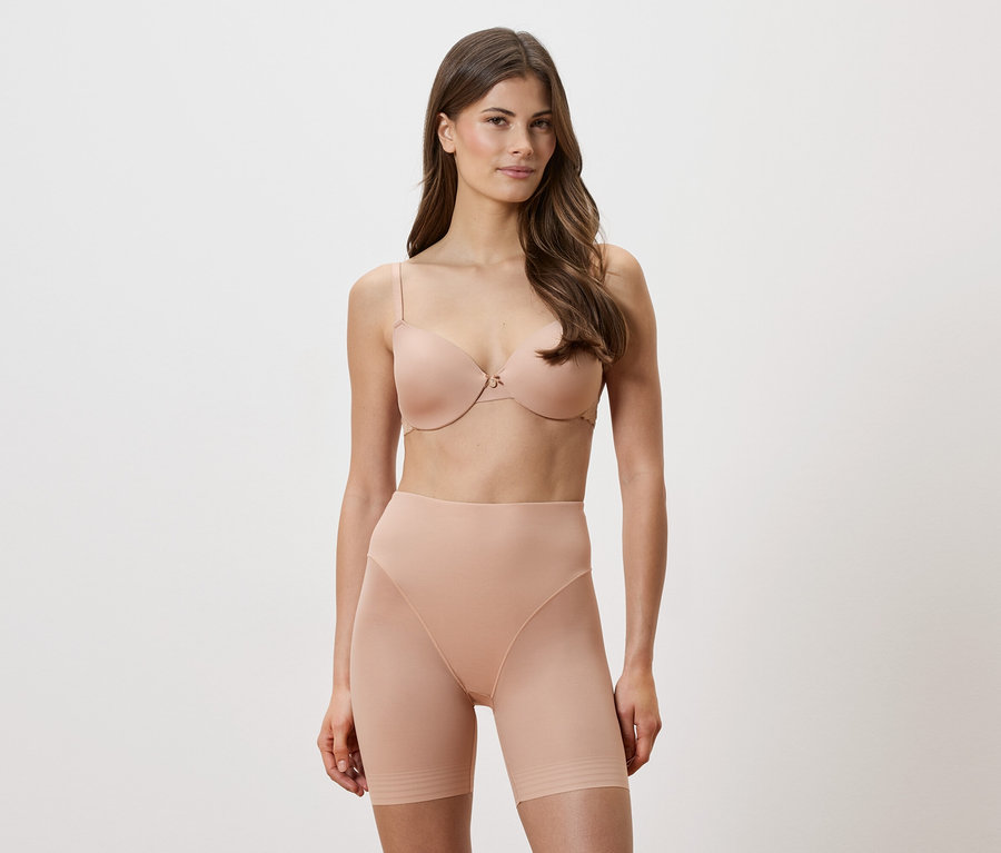 Žena má na sebe telovú podprsenku a tvarujúce šortky na bielom pozadí.