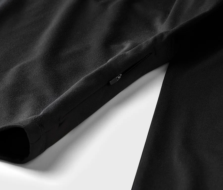 Detail čierneho odevu s rukávom a vreckom na zips na bielom pozadí.