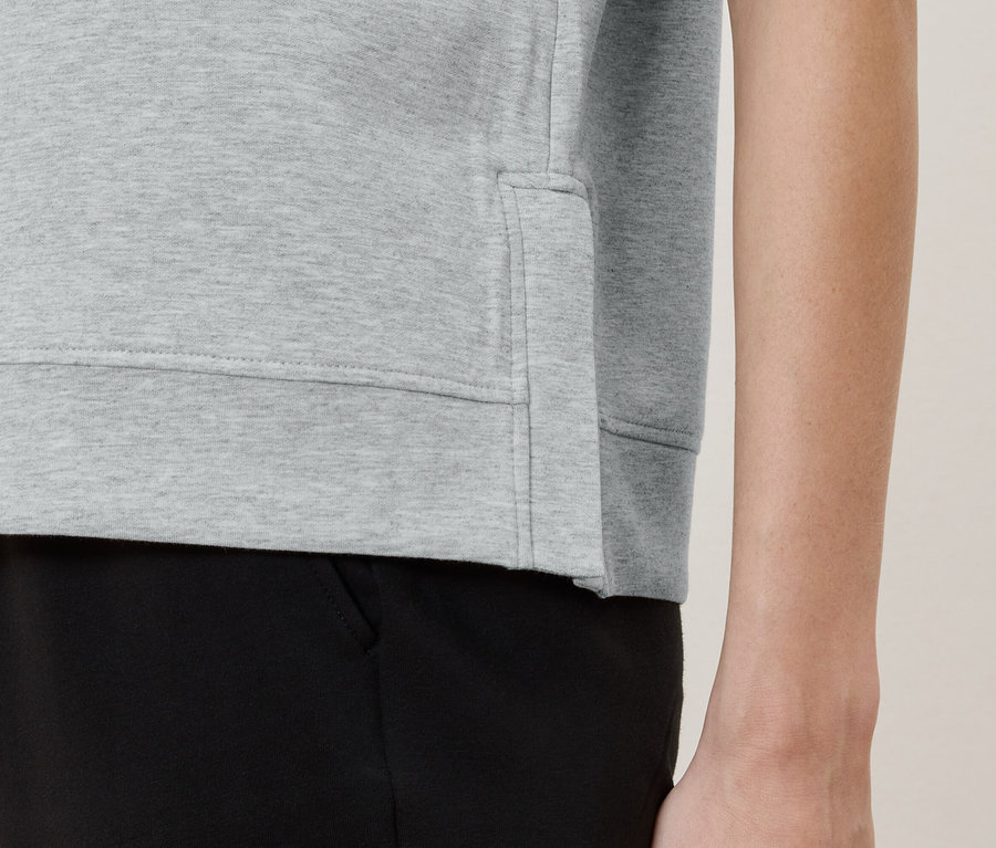 Detailný pohľad na osobu v svetlosivom svetri a čiernych nohaviciach.