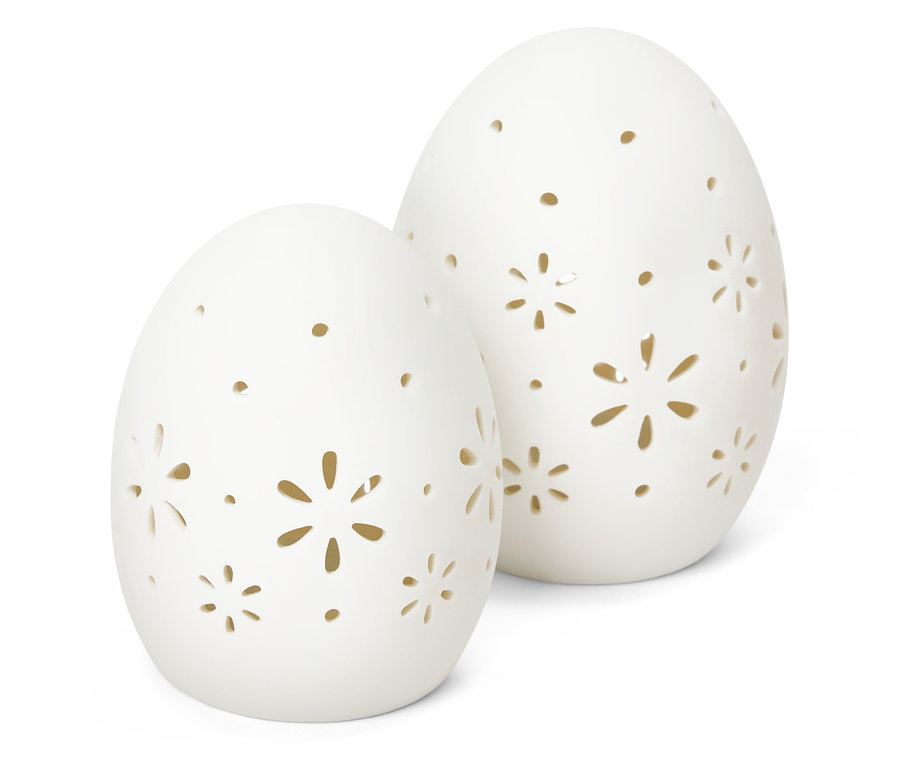 Dve biele dekoratívne vajíčka s vyrezanými kvetinovými vzormi stoja na bielom pozadí.
