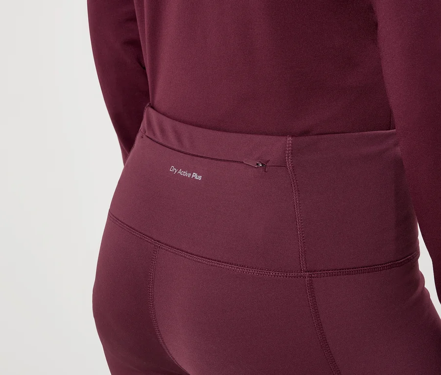 Detailný záber ženy v bordových legínach a tope s dlhým rukávom s nápisom „Dry Active Plus“.