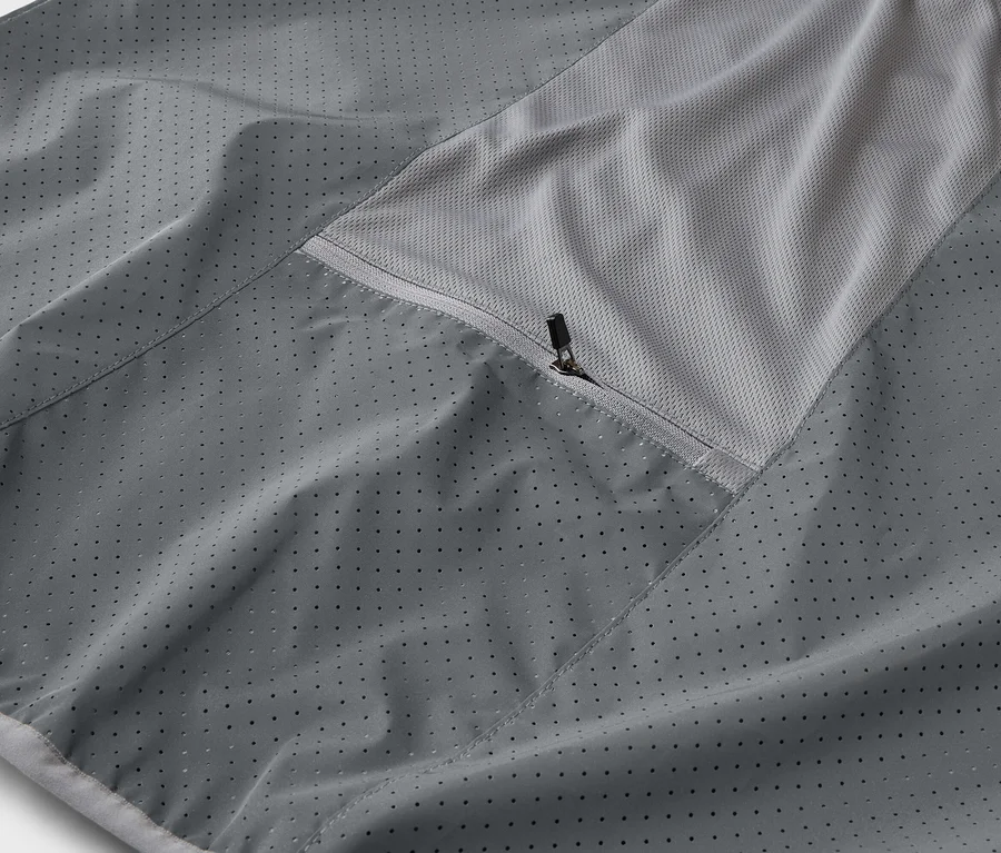 Detail šedej bundy s vreckom na zips a priedušnou sieťovanou vložkou.