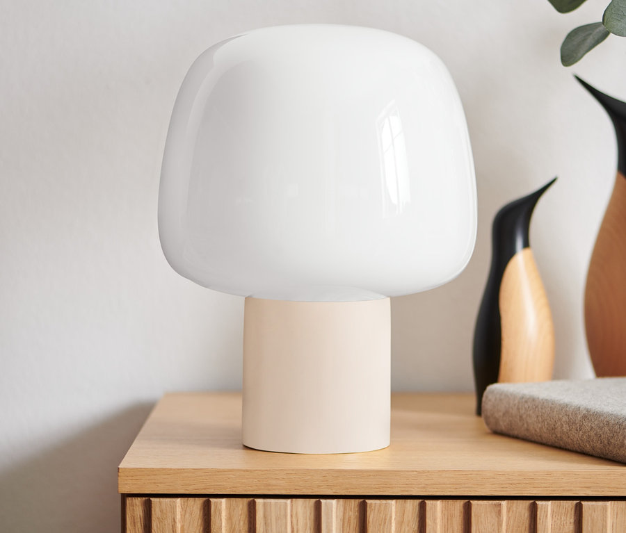 Na drevenom stolíku stojí stolová lampa s LED a akumulátorom, vedľa nej sú dekoratívne predmety vrátane vázy s rastlinami.