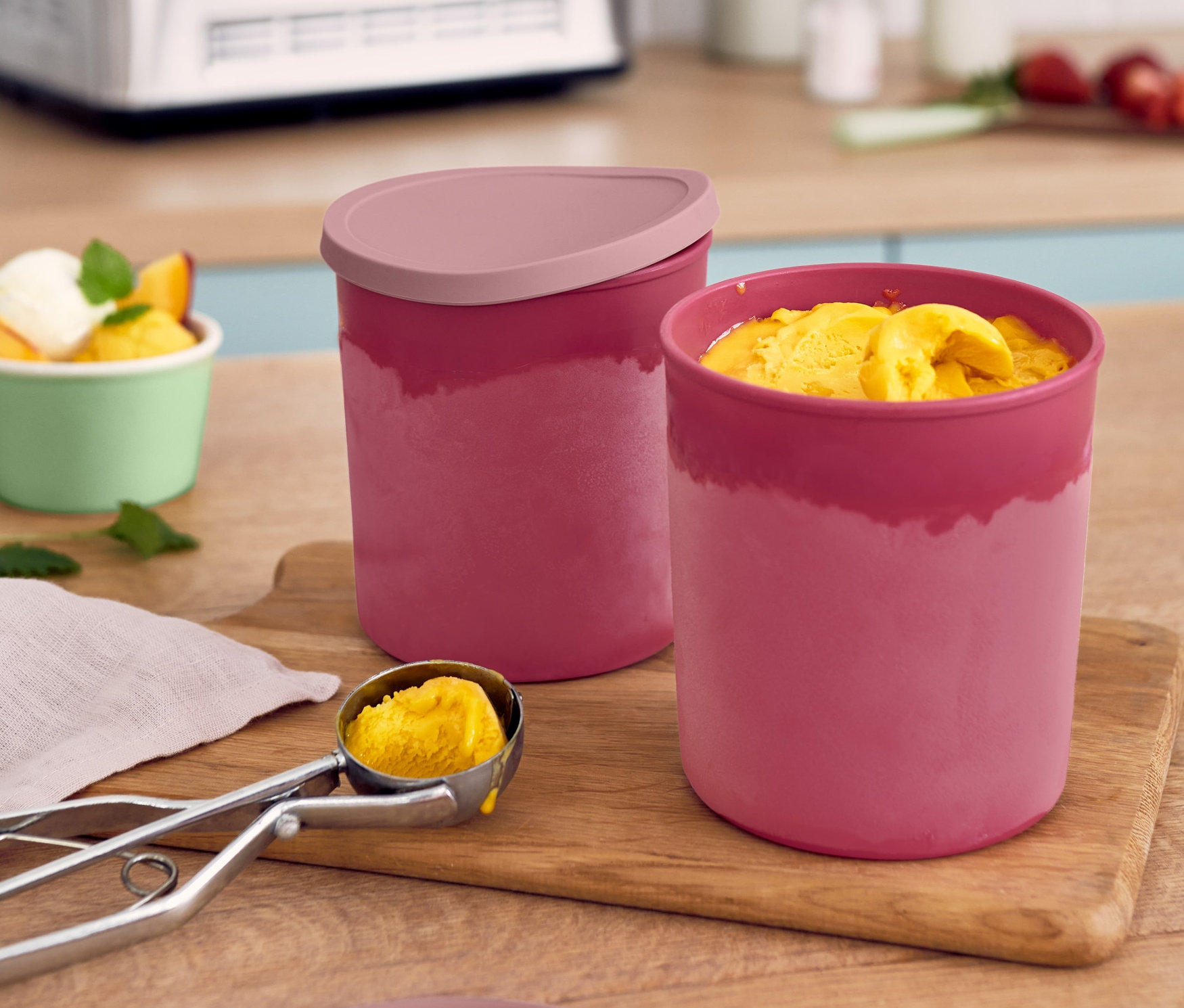 Dve červené dózy do mrazničky a lyžica zmrzliny na drevenej doske.