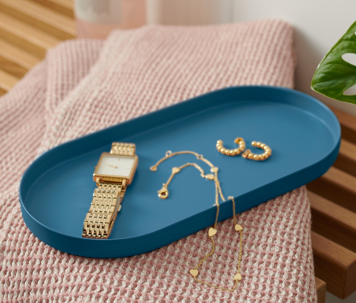 Na lavici leží modrý kovový podnos s hodinkami a šperkami.