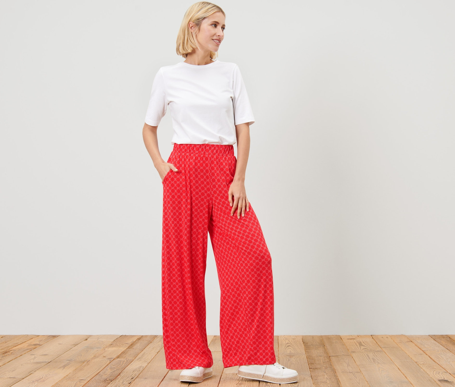 Žena stojí a pózuje v červených vzorovaných širokých nohaviciach.
