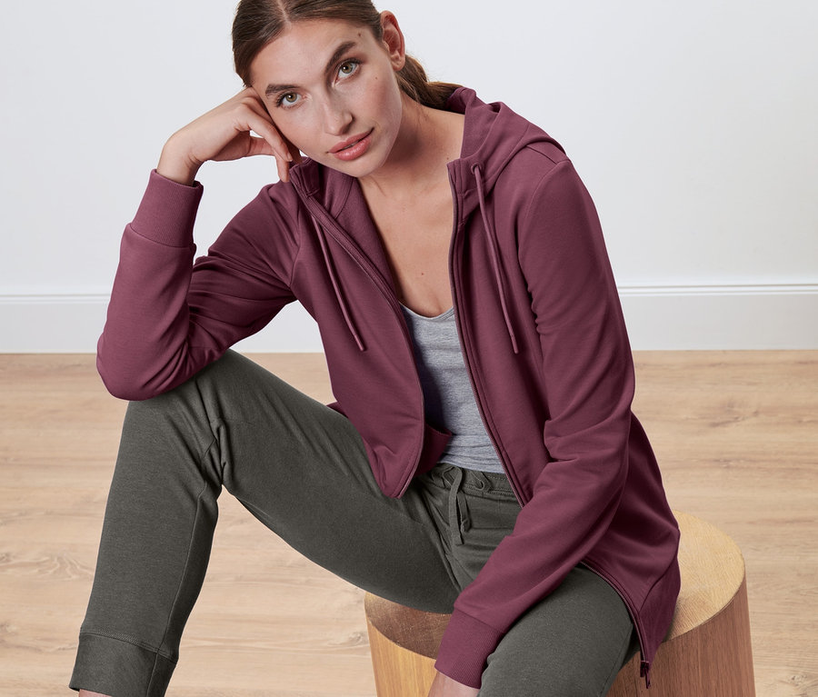 Žena sedí na drevenej stoličke a má na sebe mikinu.