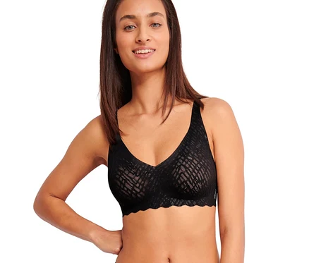Usmievavá žena v čiernej podprsenke sloggi ZERO Feel Bliss Soft bra a zladených vzorovaných nohavičkách, s rukou na boku.