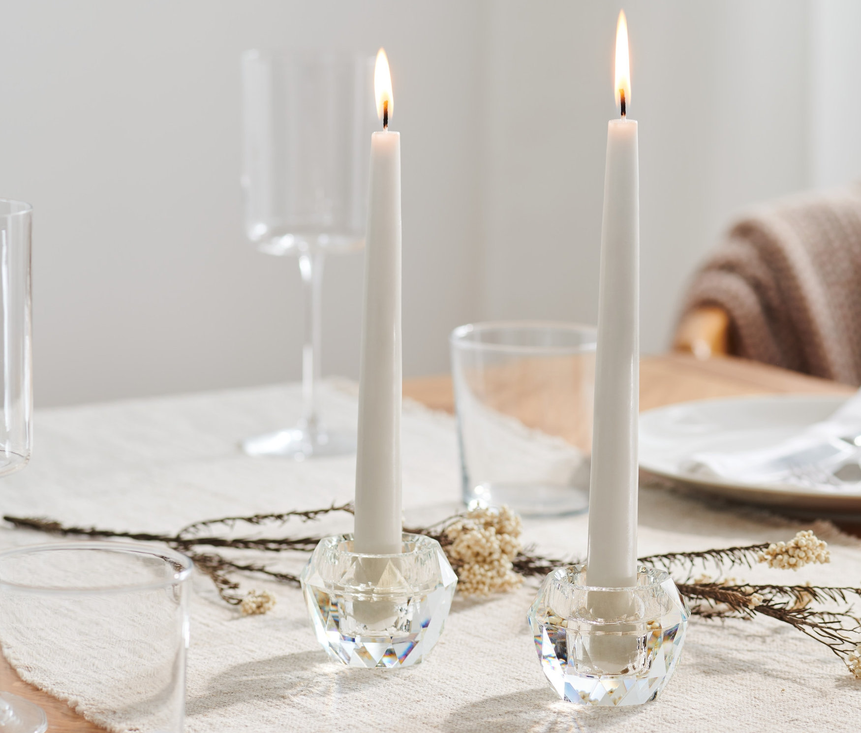 Dva sklenené svietniky so zapálenými sviečkami na stole.