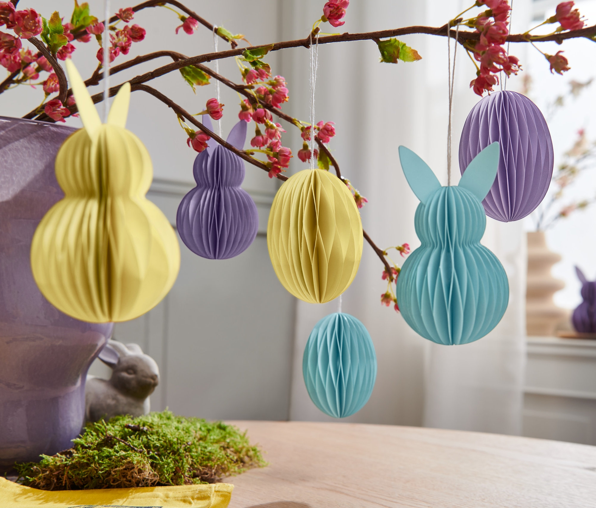 Žlté, fialové a modré papierové veľkonočné ozdoby, 6 ks, visia na kvitnúcej vetve.