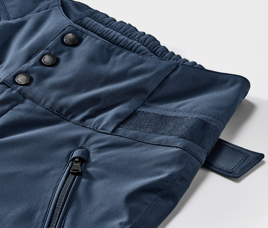 Detail modrých lyžiarskych nohavíc s vysokým pásom. Zapínanie na gombíky, zips a suchý zips.