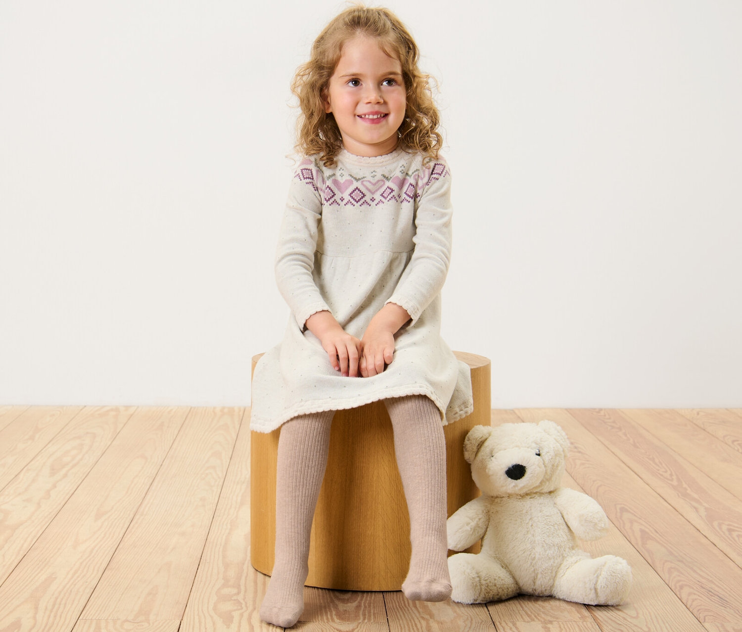 Dievča sedí na drevenej stoličke a má na sebe šaty a detské pančuchové nohavice s RWS vlnou.