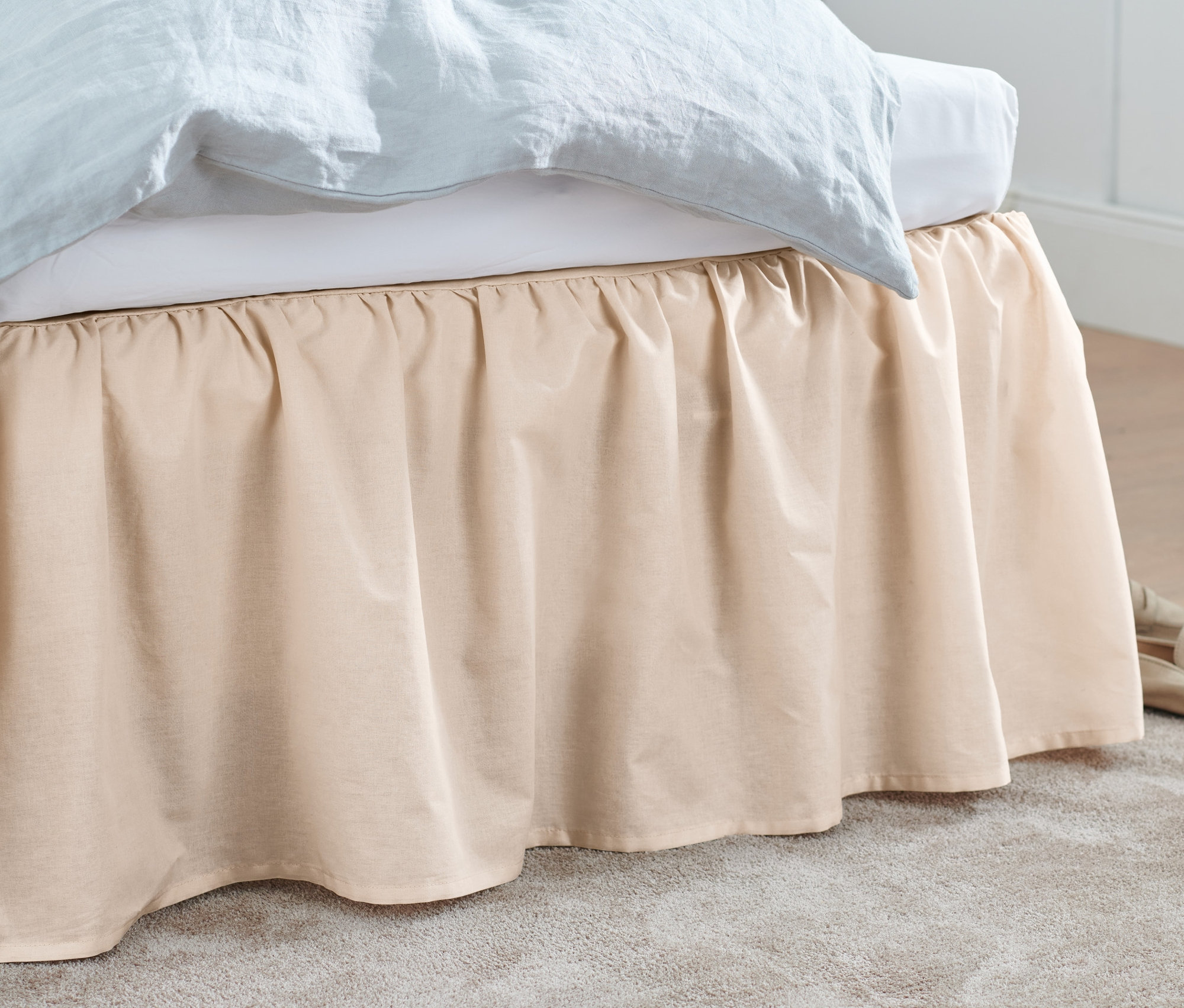 Béžová posteľná prikrývka zakrýva posteľ. Na podlahe ležia béžové topánky a sivý koberec.