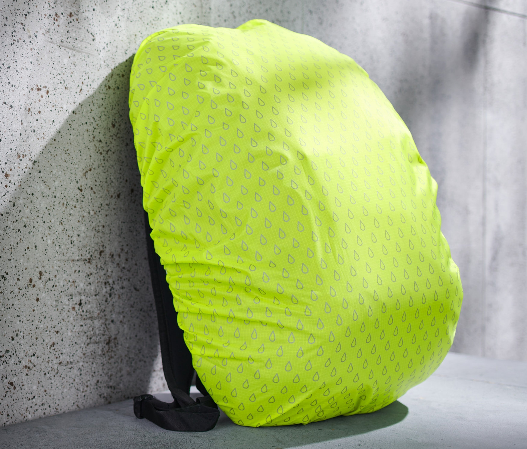 Žltý nepremokavý ochranný návlek na ruksak s potlačou kvapiek na ruksaku opretom o stenu.