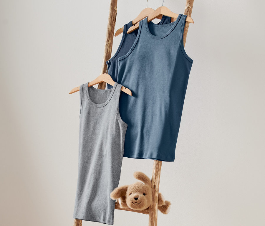 Na drevenom rebríku visia na vešiakoch sivé a modré detské tielka a plyšový psík.