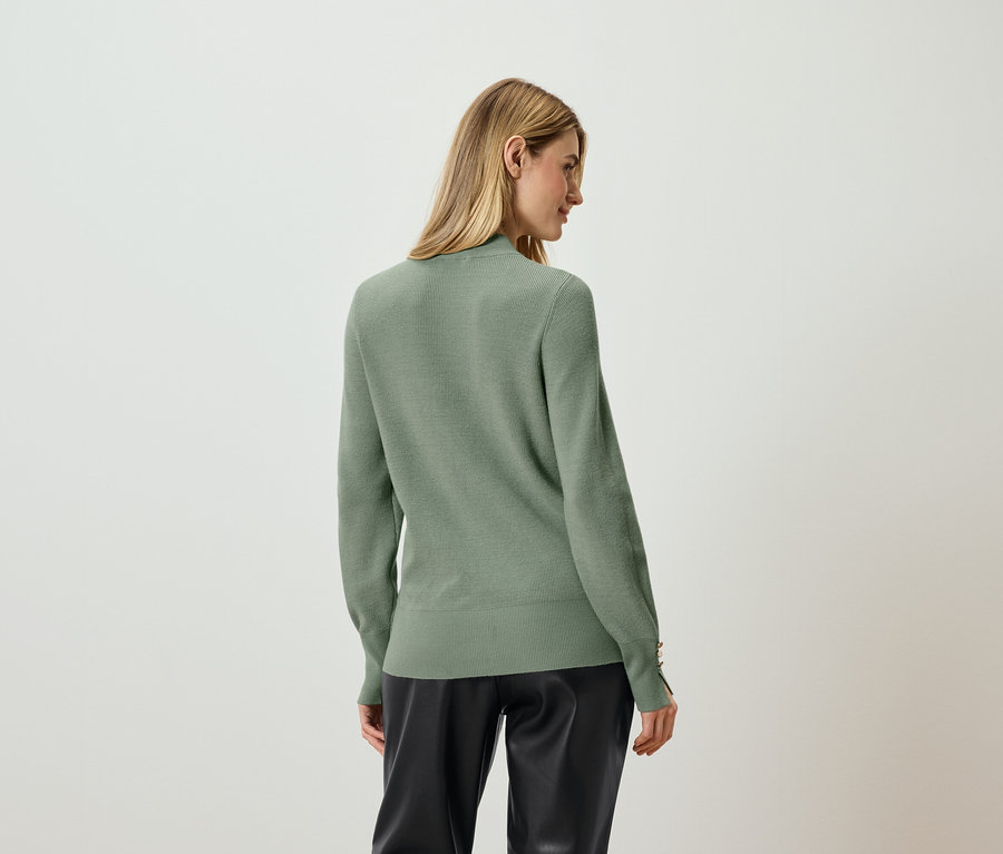 Žena stojí chrbtom a má na sebe svetlozelený sveter a čierne nohavice.