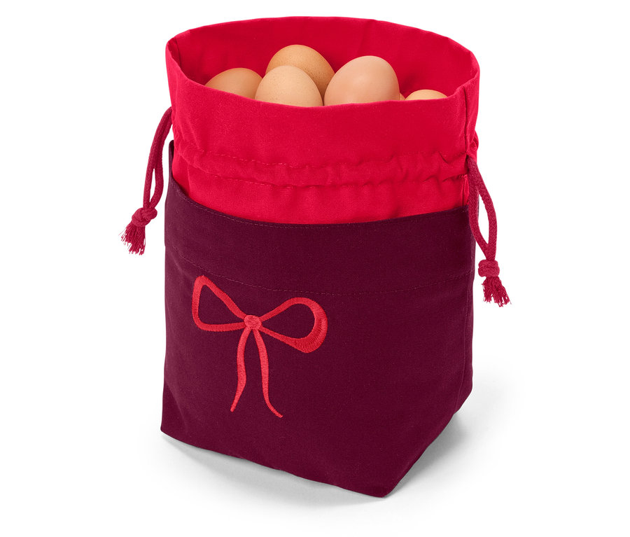 Látkový vrecúško s červeným lemom a vínnym spodkom, ozdobený výšivkou červenej mašle, plný hnedých vajec.
