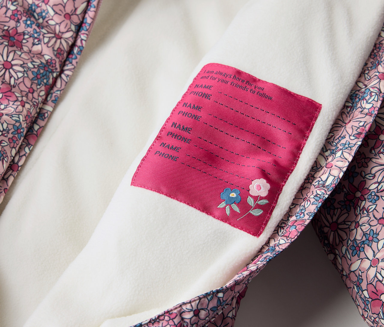 Detail zimného overalu pre bábätká s kvetinovým vzorom a štítkom na meno.