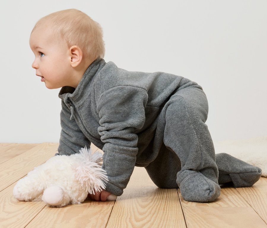Detský flaušový overal na bábätku ležiacom na bruchu vedľa plyšovej hračky.