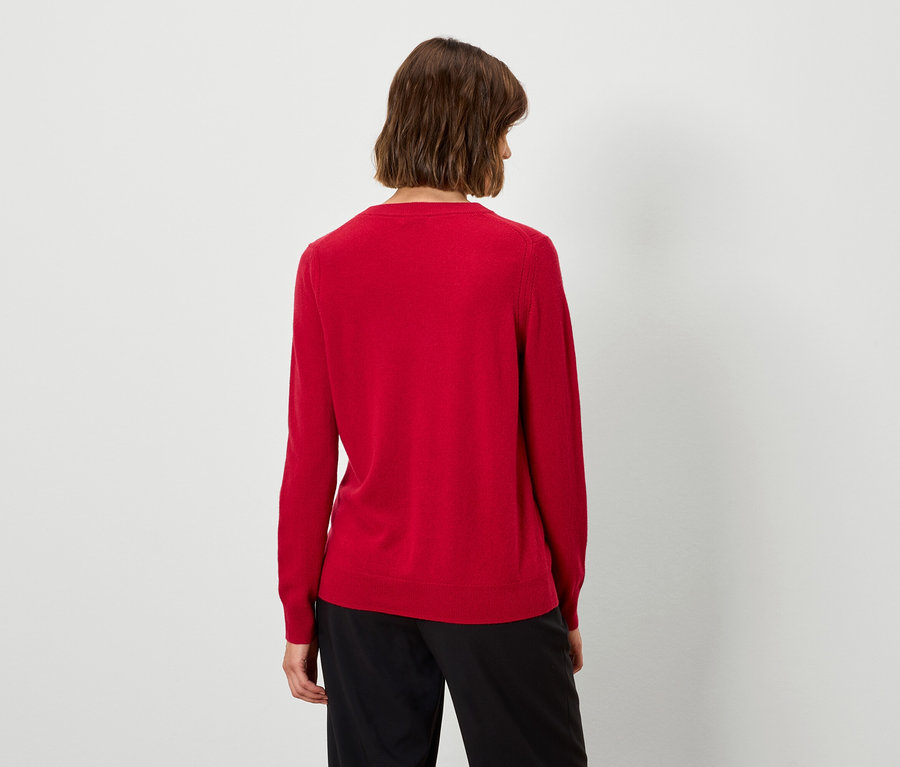 Zozadu je vidieť žena s krátkymi hnedými vlasmi v červenom svetri a čiernych nohaviciach.