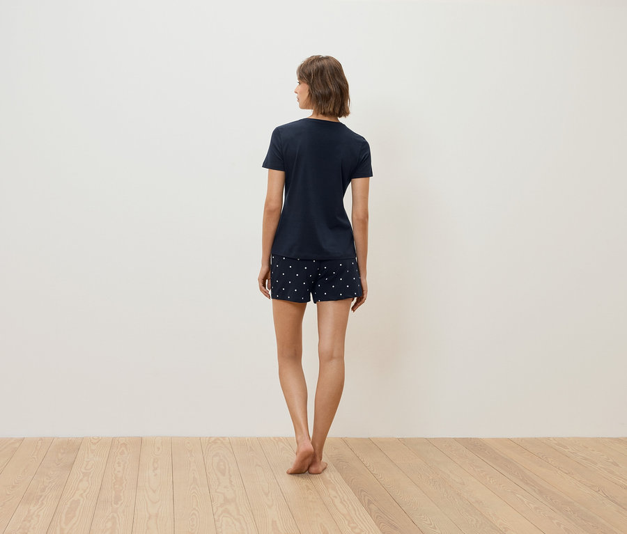 Žena stojí chrbtom k fotoaparátu a má na sebe tmavomodré tričko a šortky s bielymi bodkami.