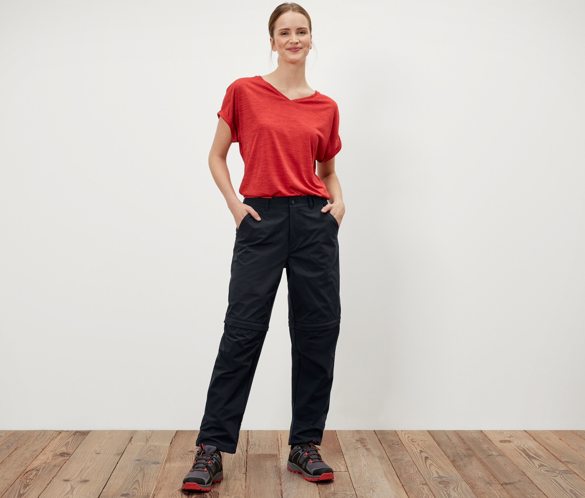 Žena stojí a má ruky vo vreckách čiernych funkčných nohavíc 2 v 1.