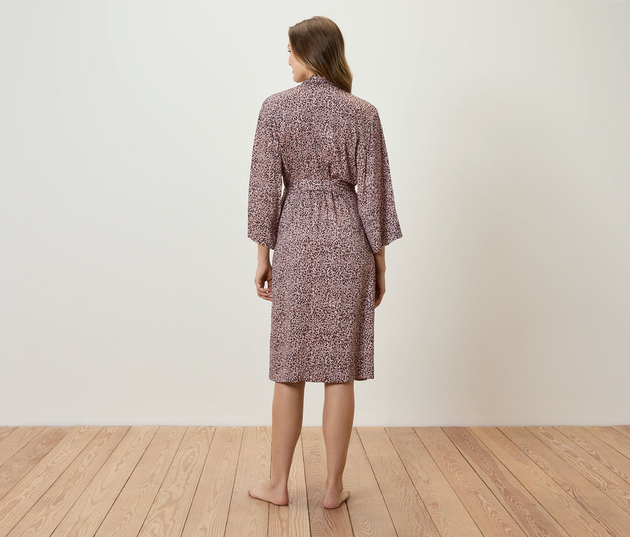 Žena stojí chrbtom k fotoaparátu a má na sebe ružový župan s potlačou.