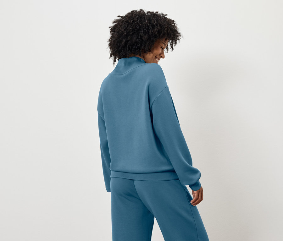 Zozadu je vidieť žena s tmavými kučeravými vlasmi v modrej mikine a nohaviciach.