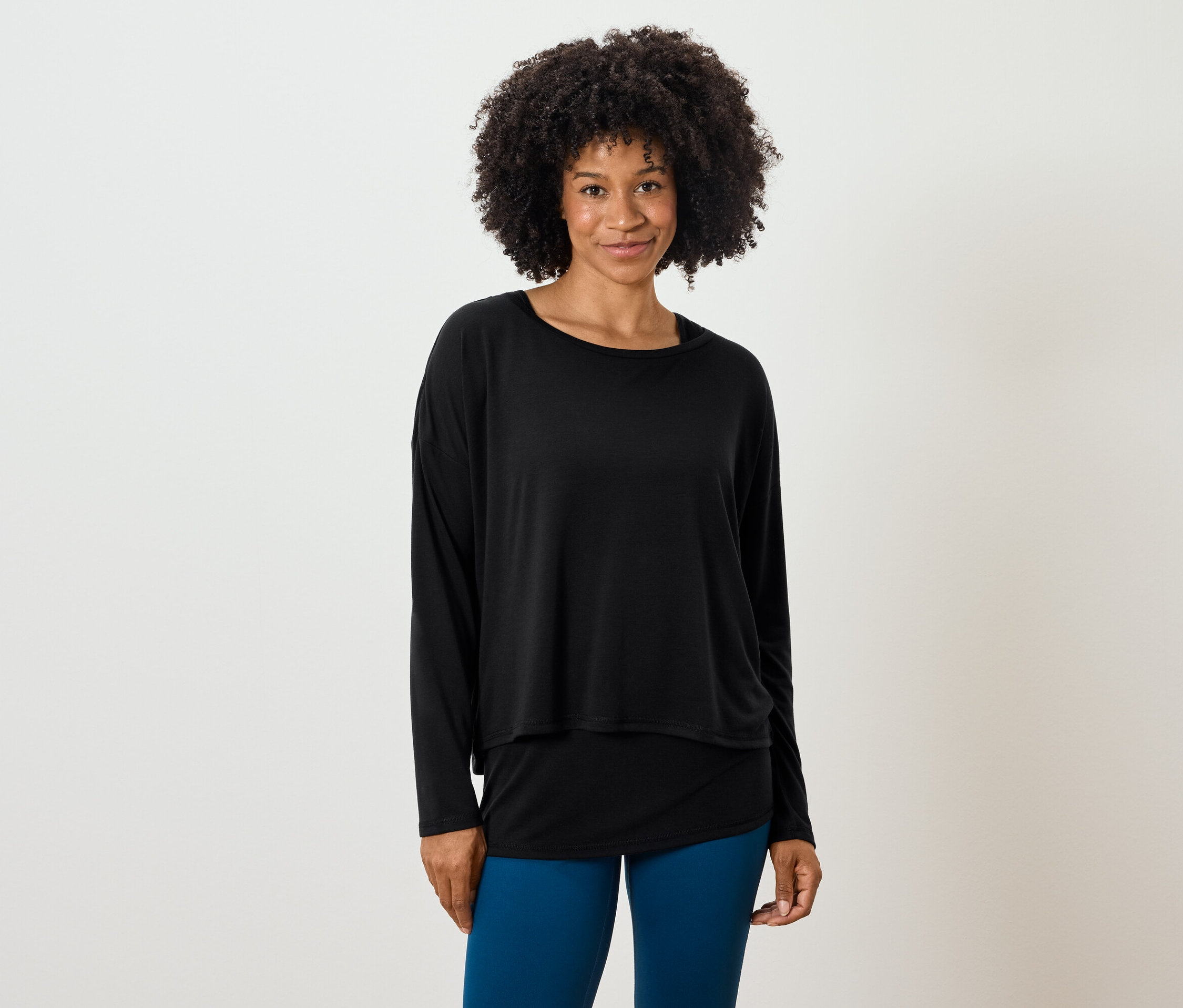 Žena s afro účesom pózuje v čiernom tope s dlhým rukávom a modrých legínach.