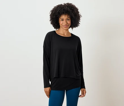 Žena s afro účesom pózuje v čiernom tope s dlhým rukávom a modrých legínach.