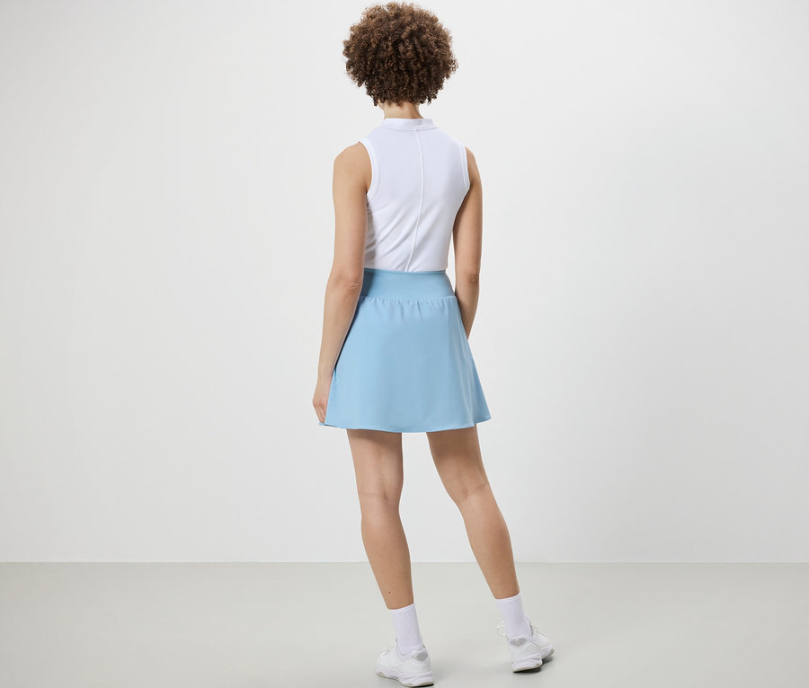 Žena stojí chrbtom k fotoaparátu a má na sebe svetlomodrú športovú sukňu.