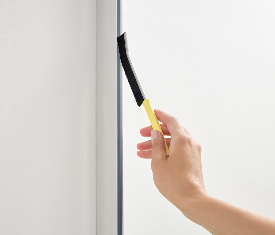 Ruka používa stierku so žltou rukoväťou na sklenenej ploche.