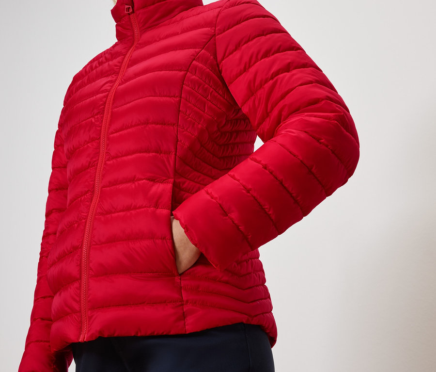 Osoba má ruku vo vrecku červenej prešívanej bundy.