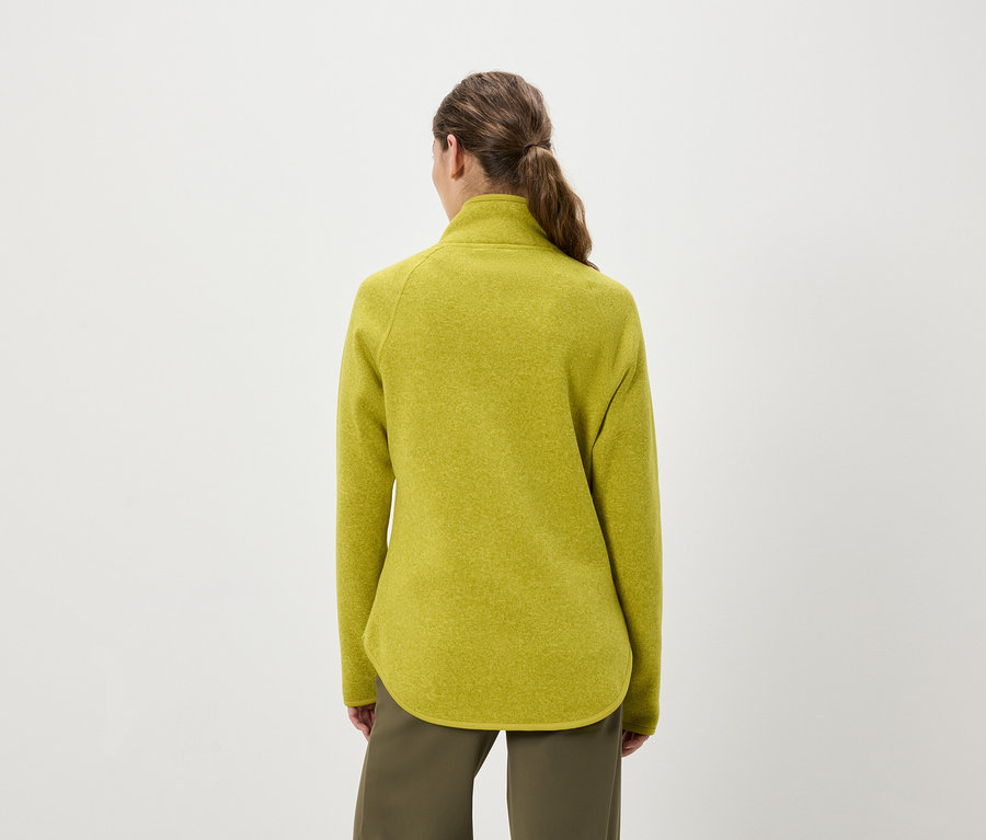 Pohľad zozadu na ženu s vlasmi stiahnutými do copu, ktorá má na sebe žltozelený flísový pulóver a olivovozelené nohavice.