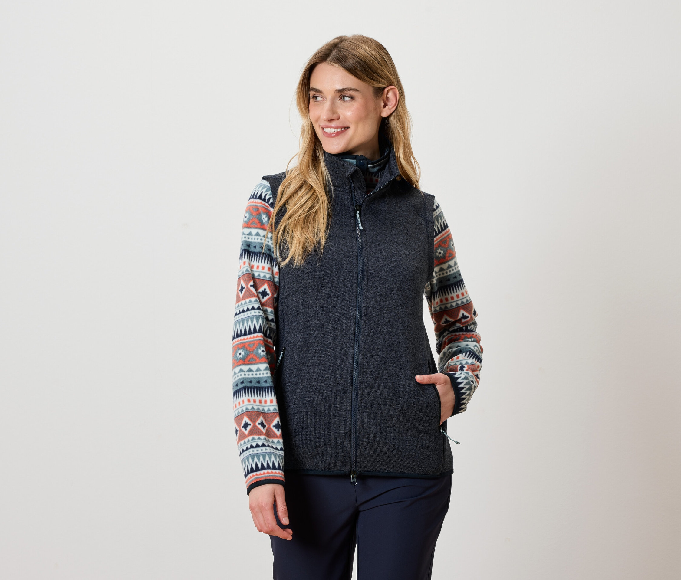 Žena má na sebe tmavosivú vestu a vzorovaný top.